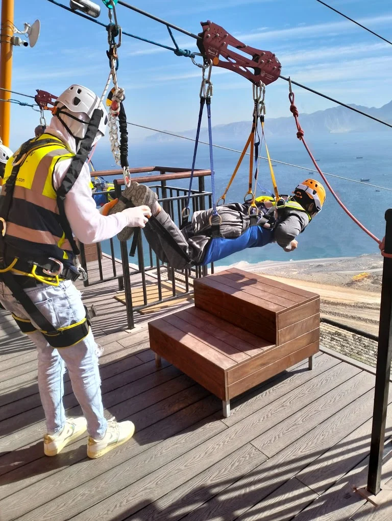 An instructor gives final instructions to a guest on the launch platform, ready to depart on the zipline high above the sea.
