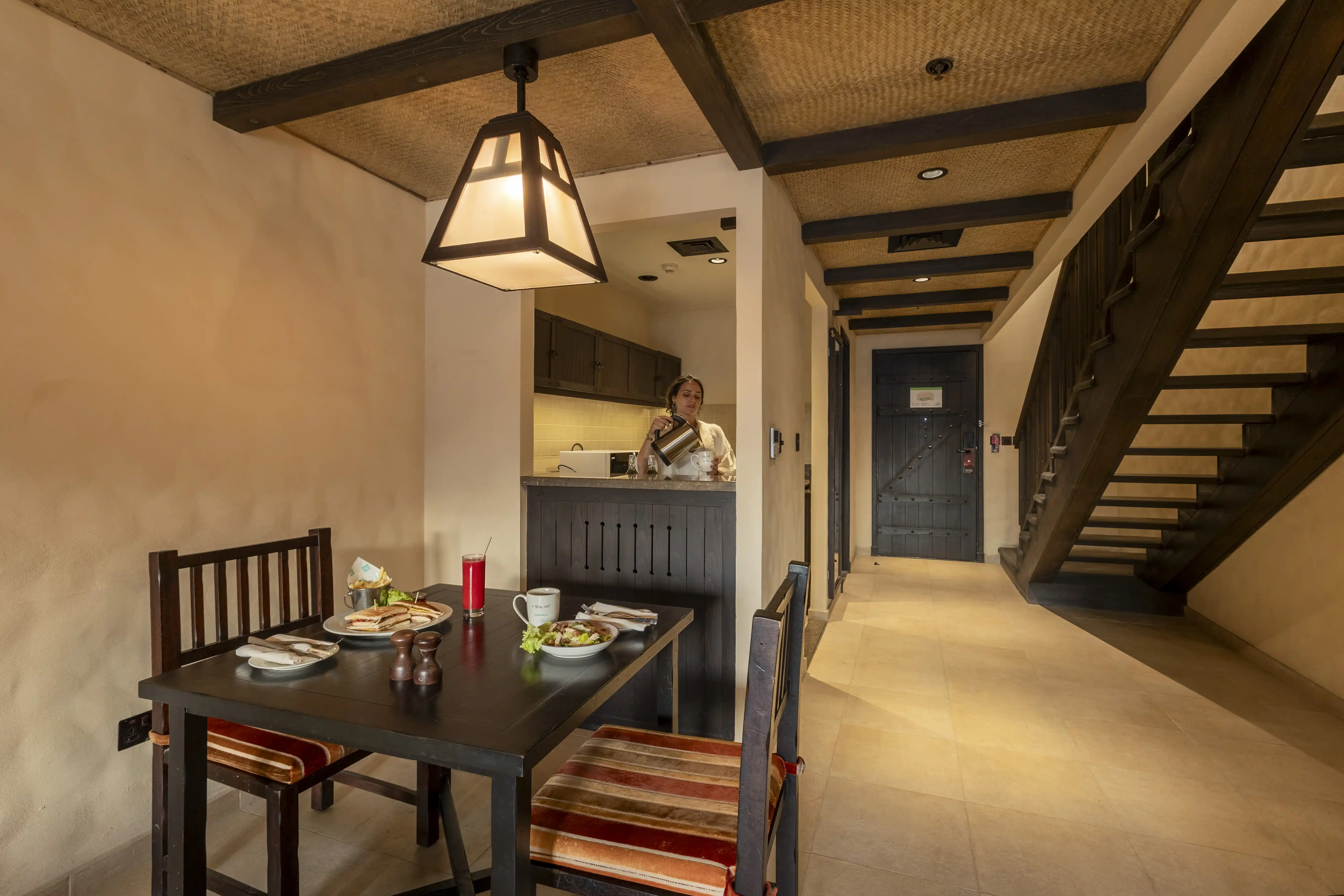 The dining area of the Duplex Room with a meal set on the table, and the kitchenette in the background where a staff member is preparing drinks.
