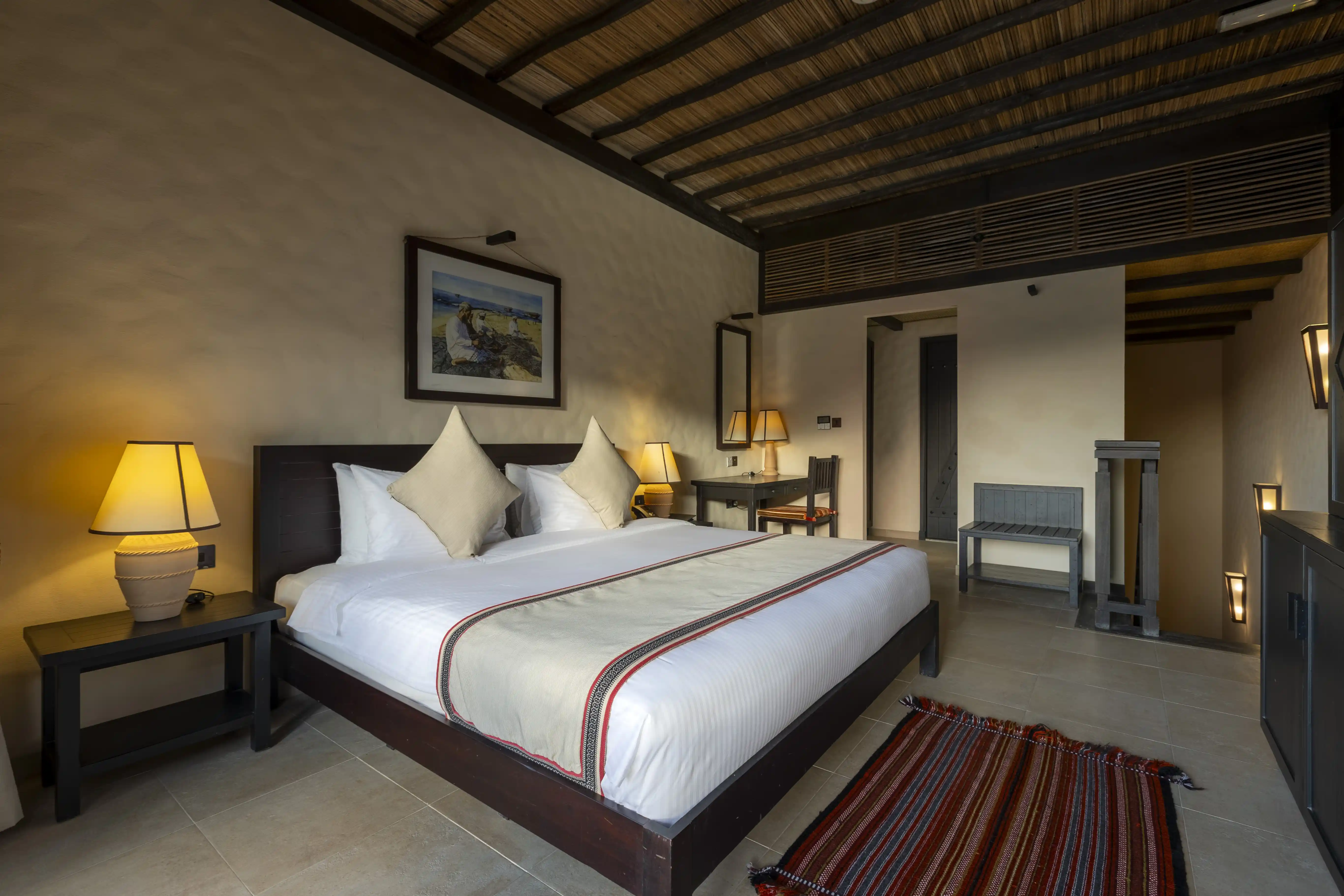 The upper level of the Duplex Room, featuring a king-sized bed and desk area, with a wooden staircase leading down to the lower level.
