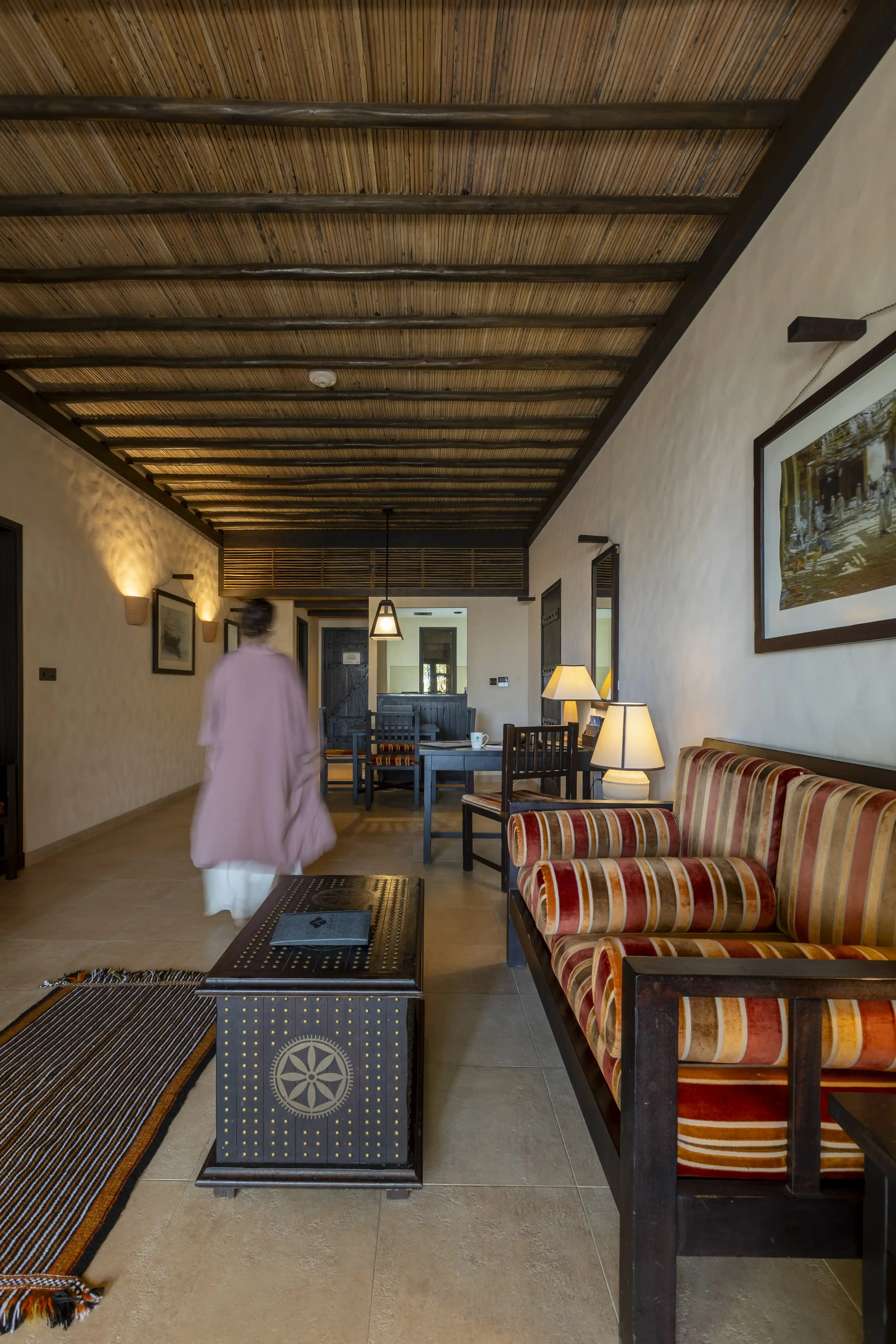 A wide view showcasing the expansive layout of the Junior Suite, looking from the living area with its striped sofa towards a guest walking through the central corridor.