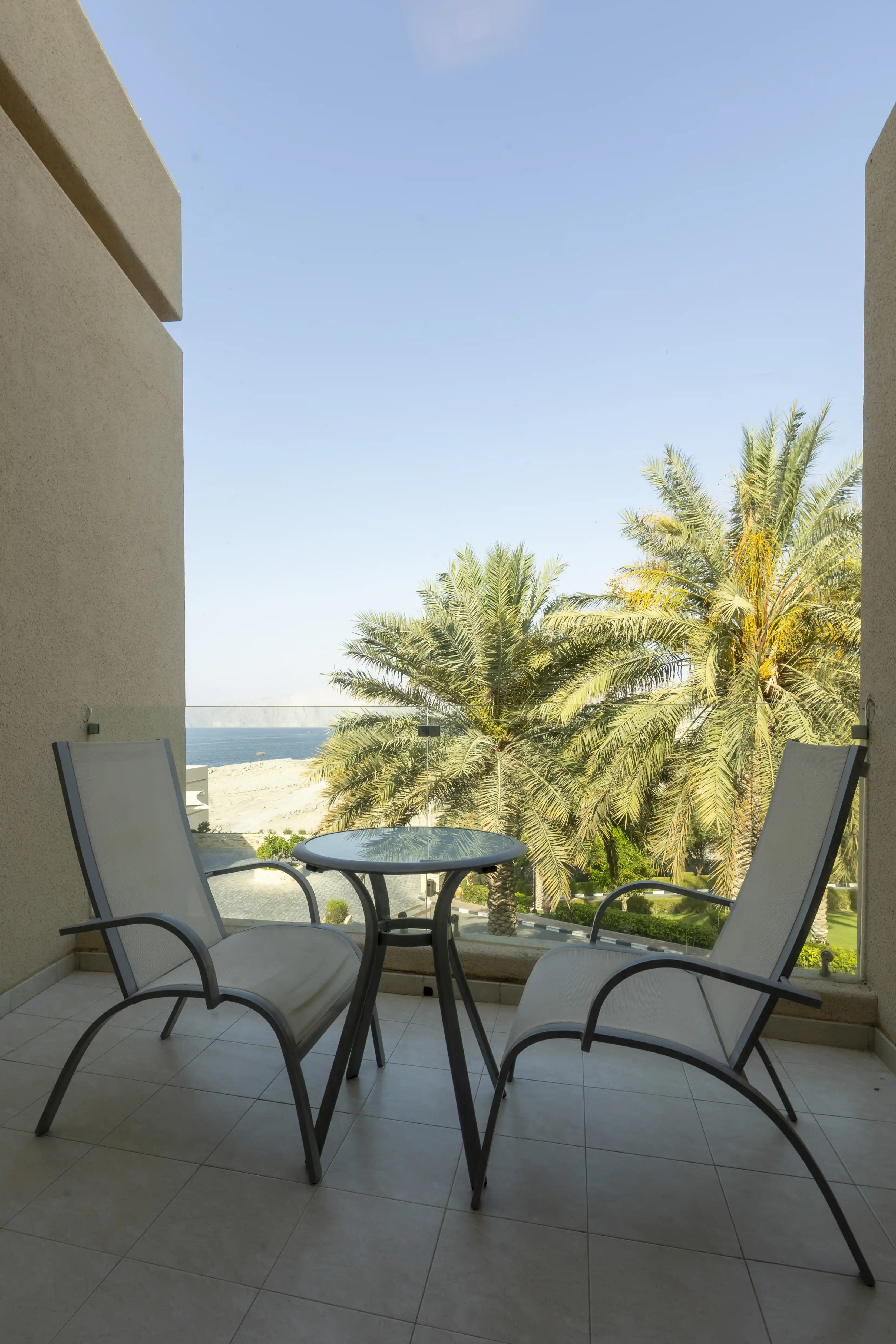 The private balcony of the King Chalet, furnished with a table and chairs and offering a view of the sea past palm trees.