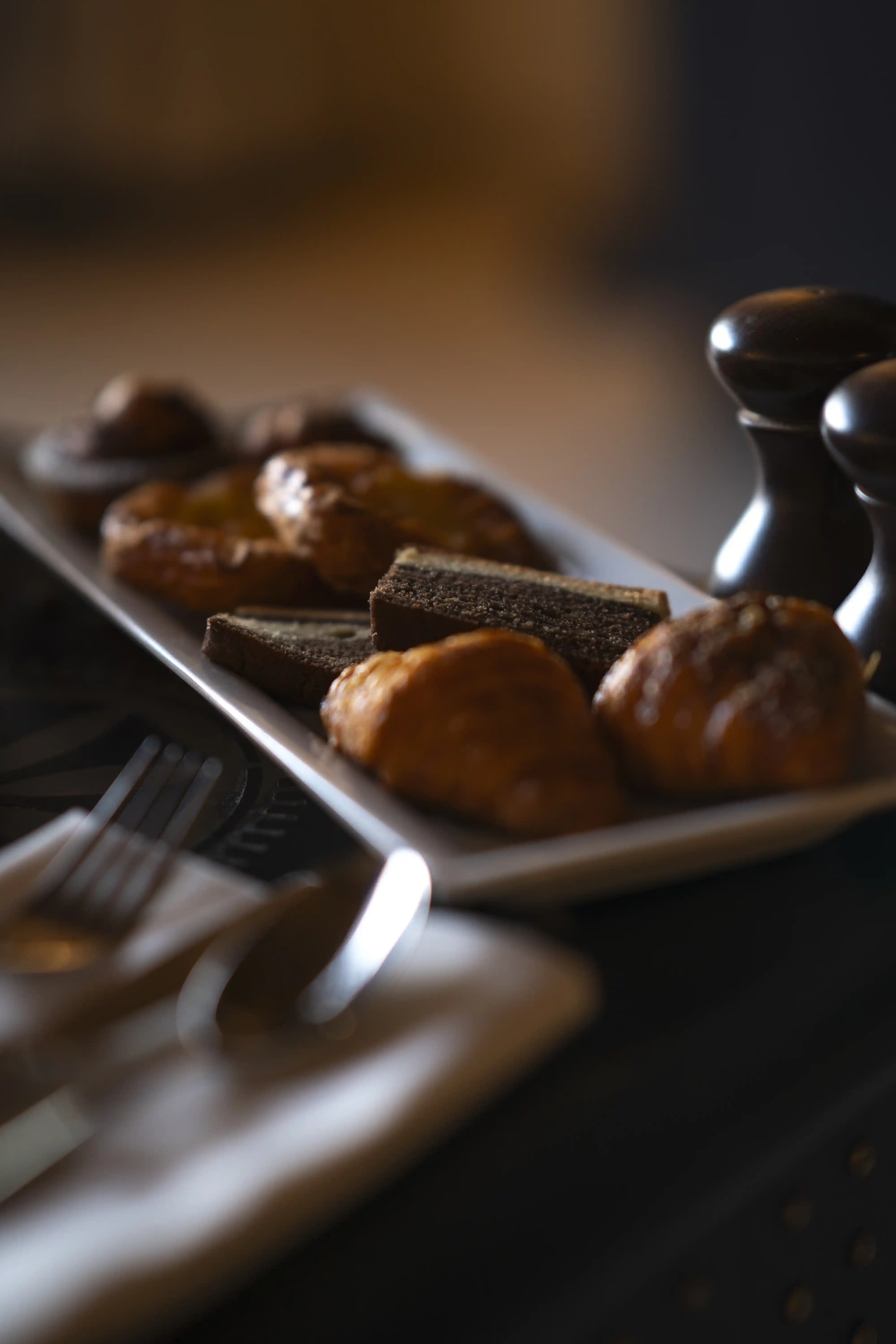 A close-up of a platter of fresh breakfast pastries, including croissants and sliced cake, served as part of an in-room dining experience.