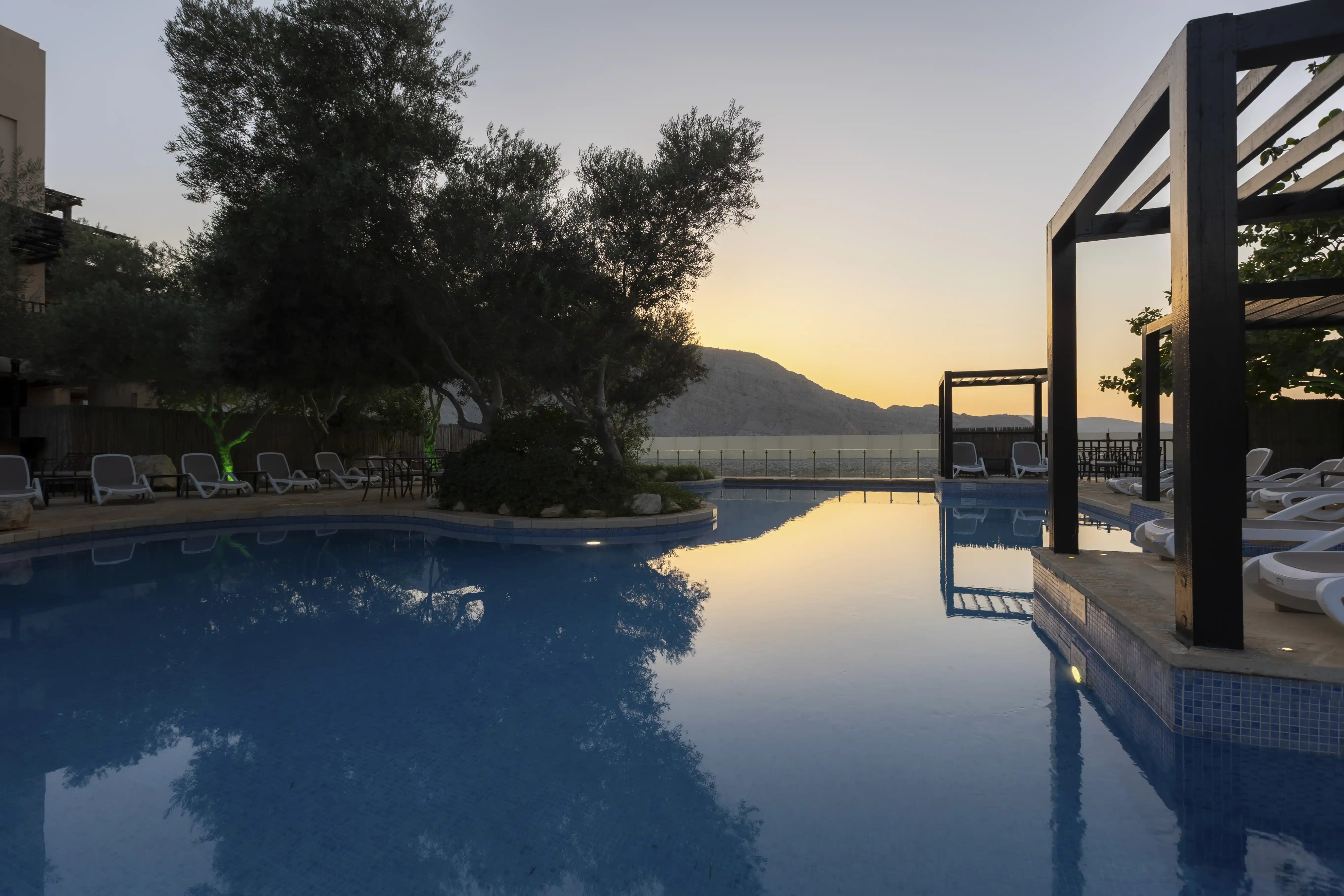 Pool of musandam, with pool side cabanas, at sunset with reflection of sun in water