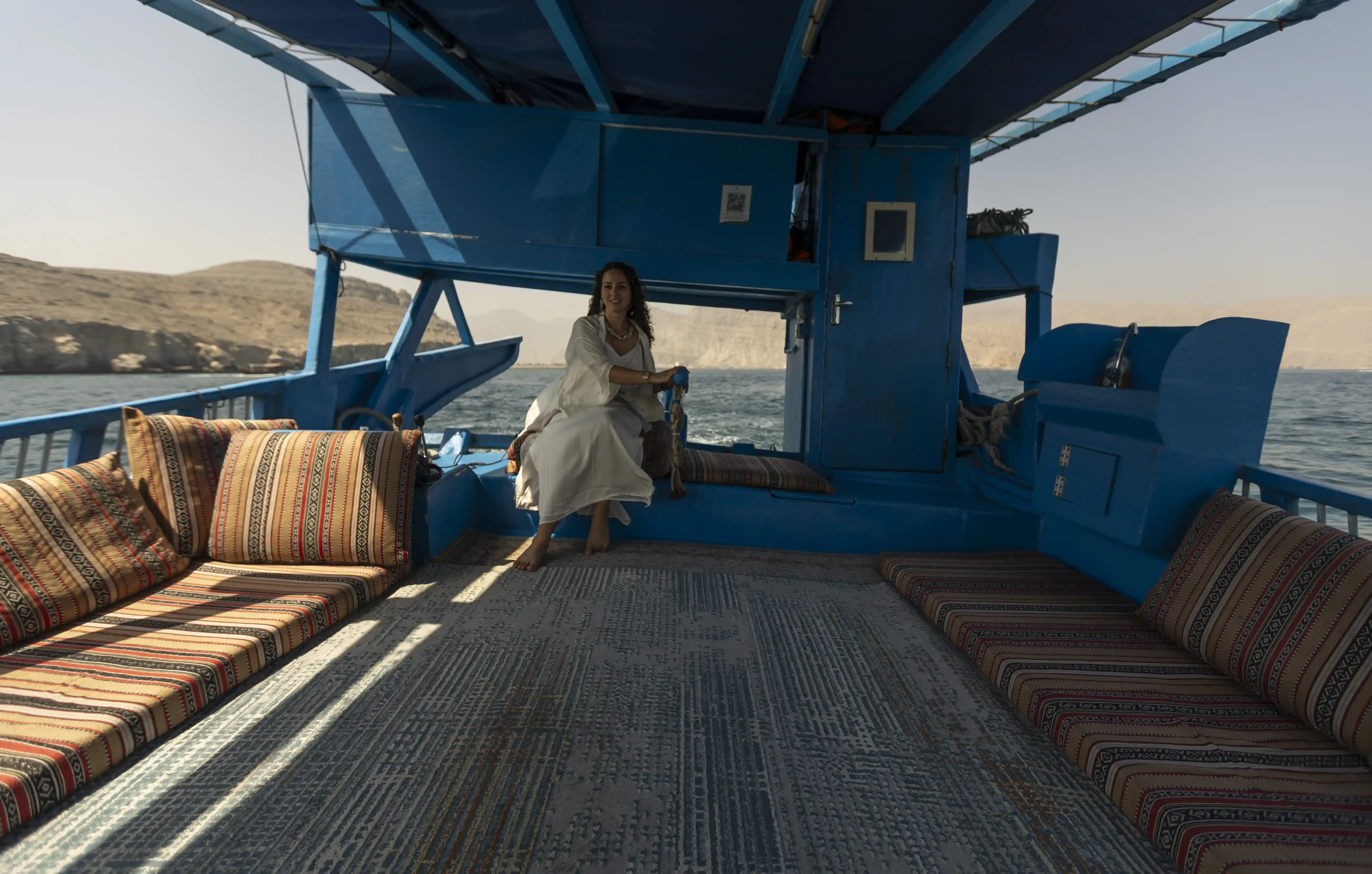 The spacious, carpeted deck of a traditional dhow boat, showing the comfortable cushioned seating where guests can relax.