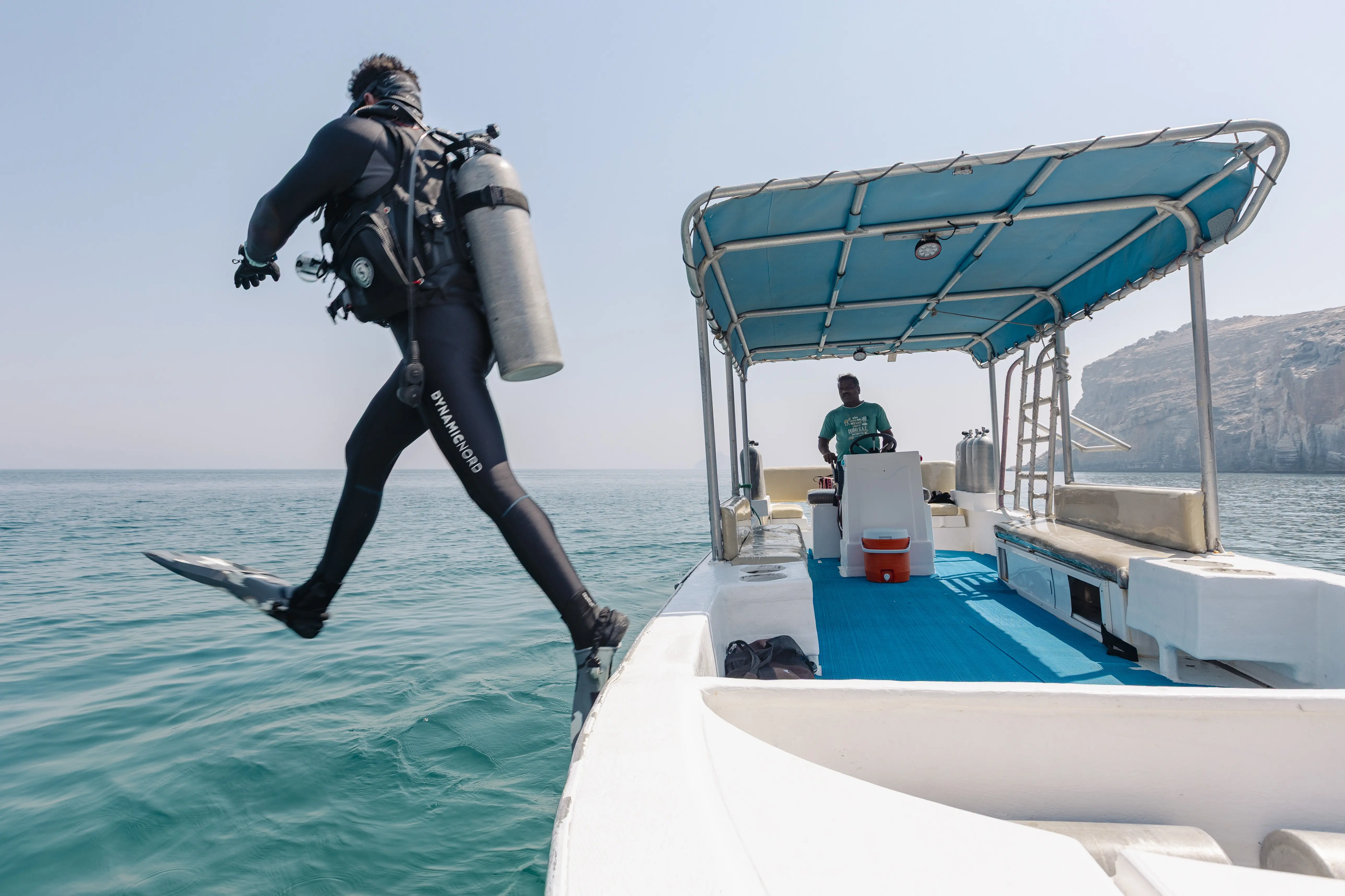 A scuba diver performs a giant stride entry into the water from the side of a dive boat.