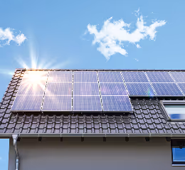 Solarmodule auf einem geneigten Hausdach unter blauem Himmel mit Sonne und Wolken.