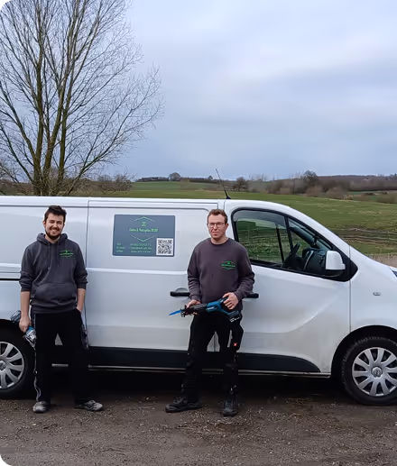 Zwei Männer stehen neben einem weißen Firmenfahrzeug mit grünem Logo und Kontaktdaten, ländliche Landschaft im Hintergrund.