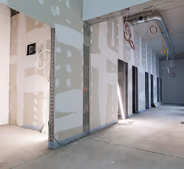 Unfertiger Innenraum mit Gipskartonwänden und sichtbaren elektrischen Leitungen in einem Neubau.