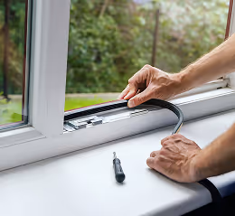 Person montiert eine schwarze Fensterdichtung an einem weißen Kunststofffenster mit Schraubenzieher auf der Fensterbank.