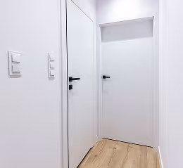 Schmaler Flur mit weißen Wänden, Holzboden und zwei weißen Türen mit schwarzen Griffen.
