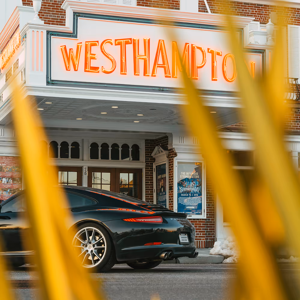 Black car in front of a white building with a Westhampton neon sign