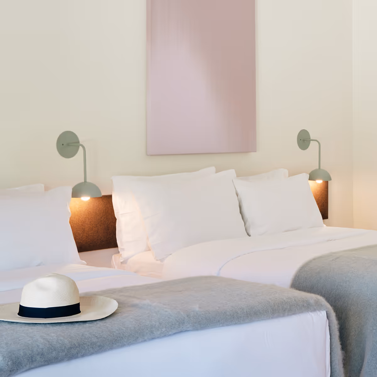 Two queen beds with paintings above and a hat resting on one bed