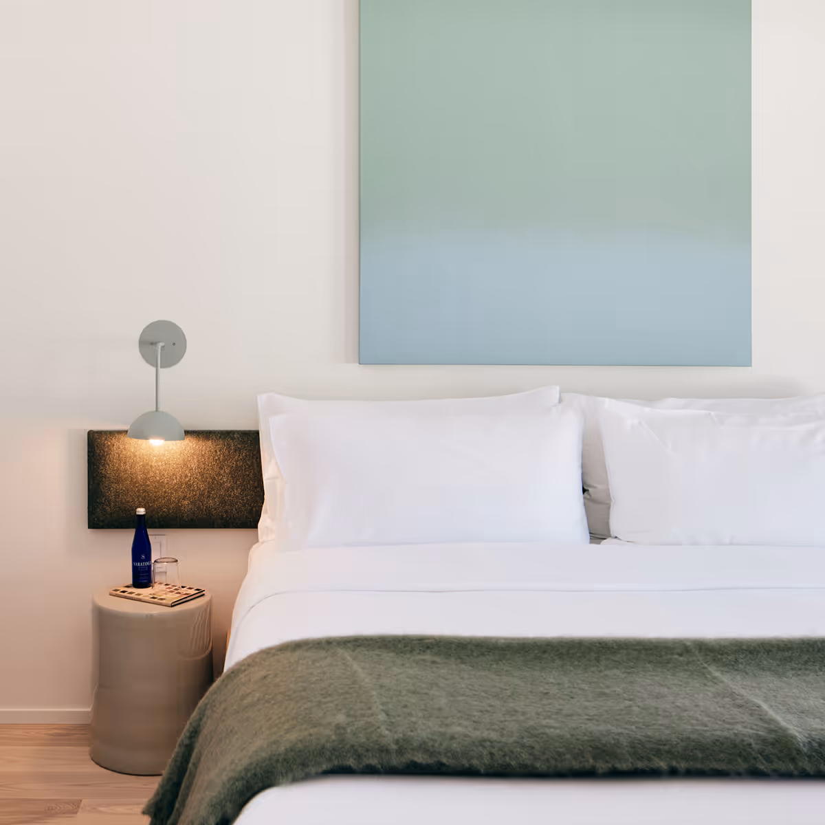 King bed with side table and sconce on the left and painting above the bed