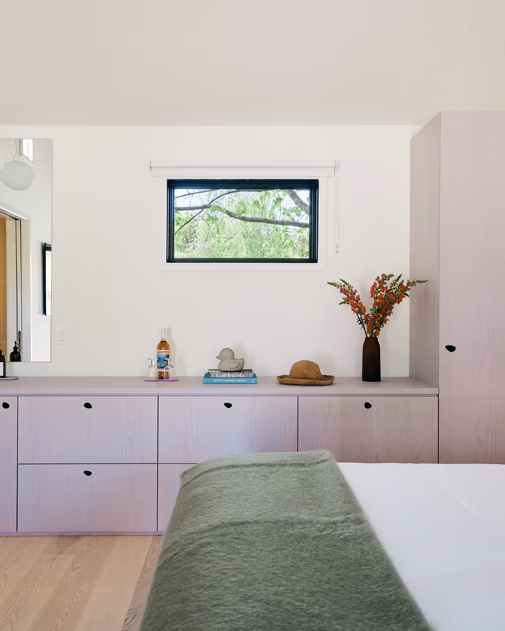 Edge of king bed overlooking dresser wall with small window