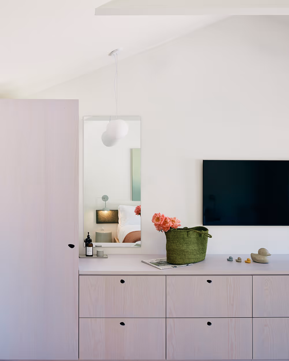 Dresser wall with drawers on top of which sits a basket with flowers and hotel products, TV and mirror mounted on wall