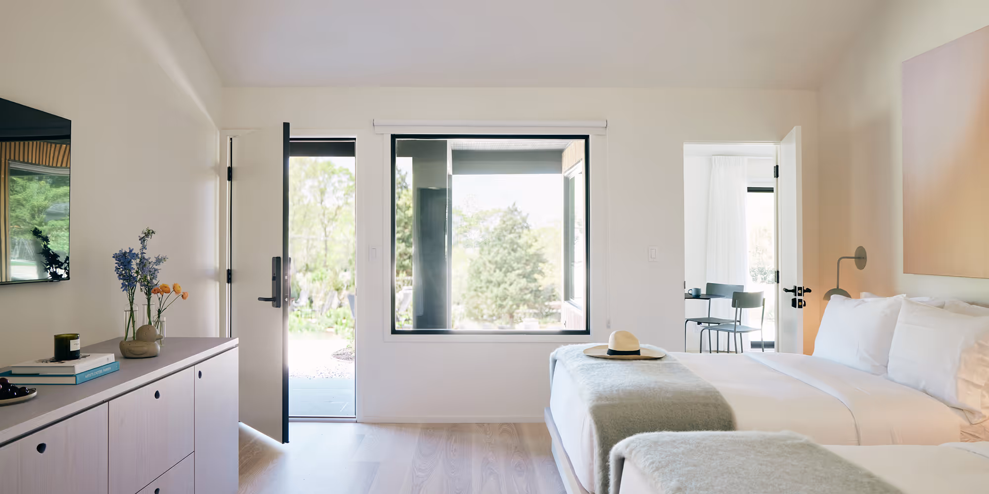 Side view of two queen beds looking towards a wall with a door on the left leading outside and a door on the right leading to a private patio