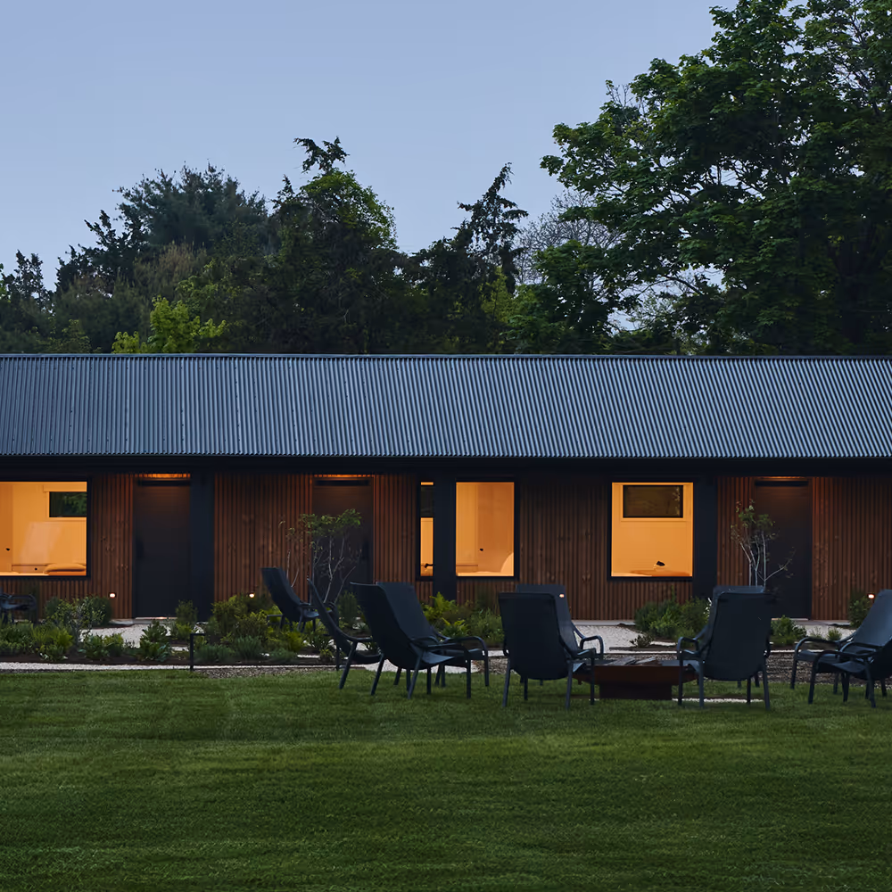 Evening view of chairs surrounding a fire pit on a grassy lawn in front of the hotel buildings