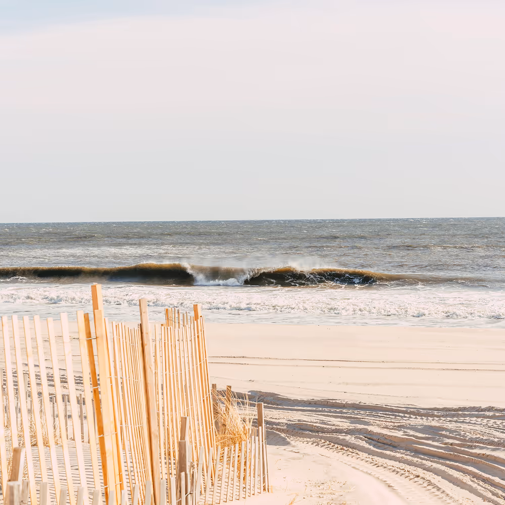Sandy path with fence on the left leading to the beach, waves crashing on the shore