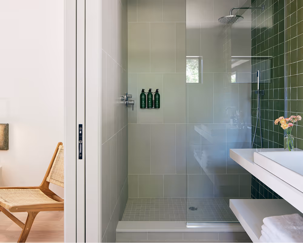 Split view of bedroom with a chair to the left and doorway into bathroom with view of the shower