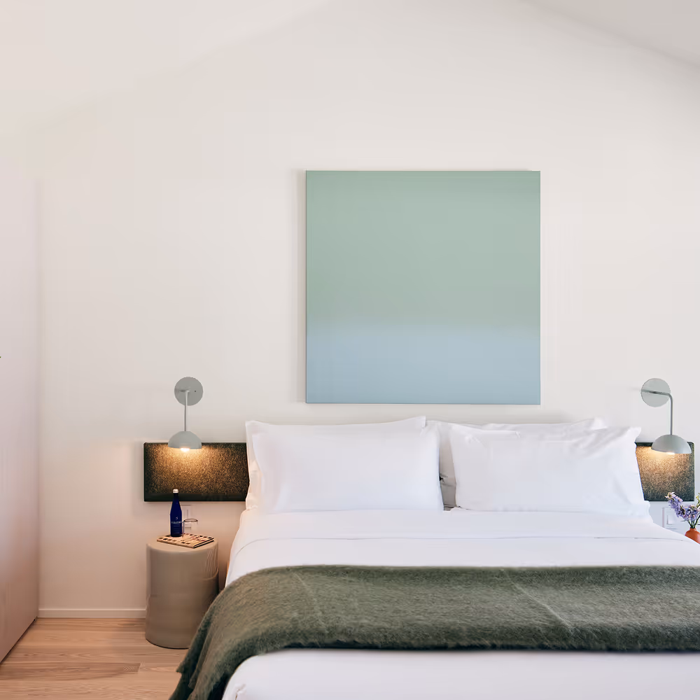 King bed with side table and sconce on the left and painting above the bed