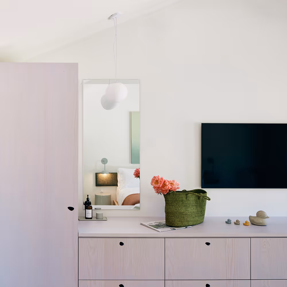 Dresser wall with drawers on top of which sits a basket with flowers and hotel products, TV and mirror mounted on wall
