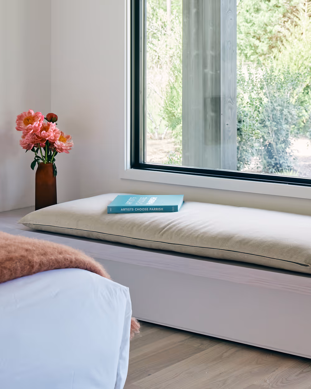 Edge of king bed with bench against wall with a large window