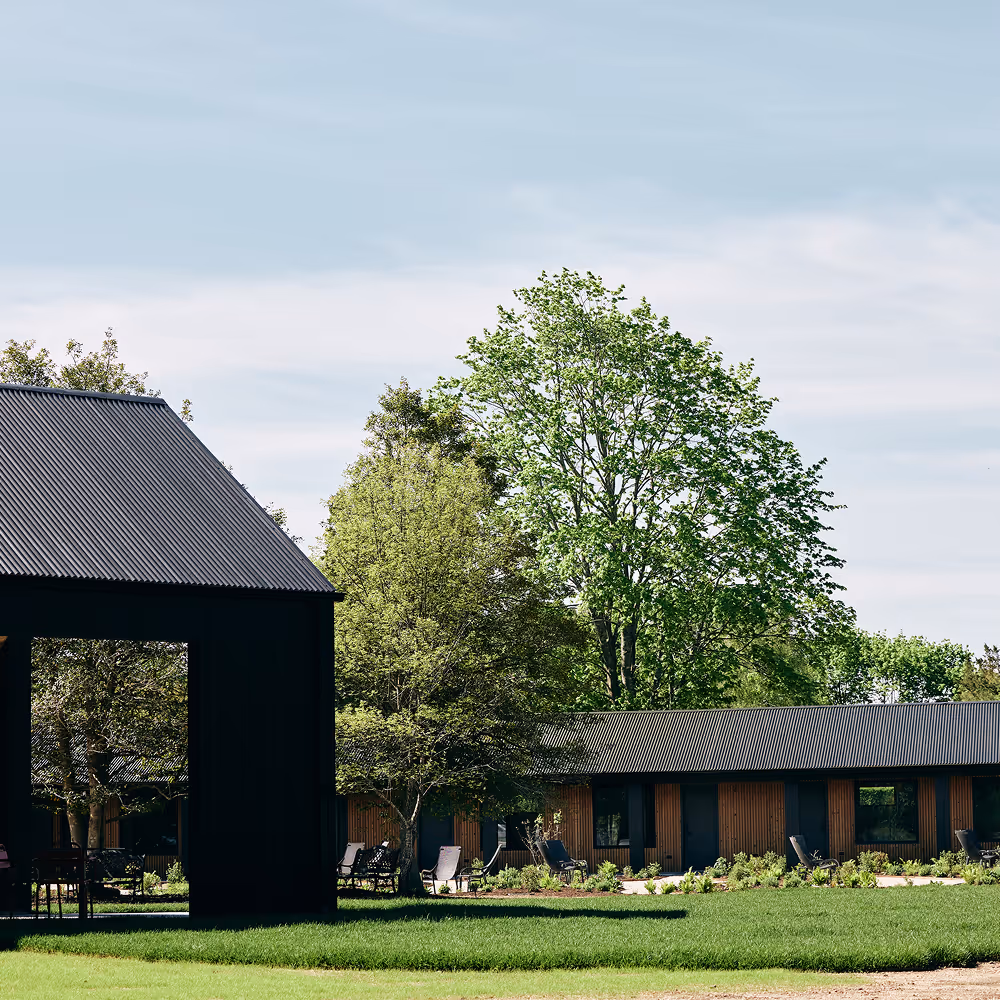 Black hotel building on a grass lawn with wood panel hotel building with black accents and trees in distance