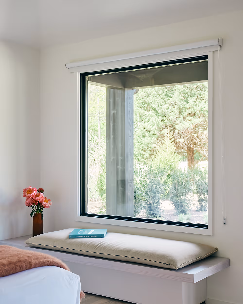 Edge of king bed with bench against wall with a large window