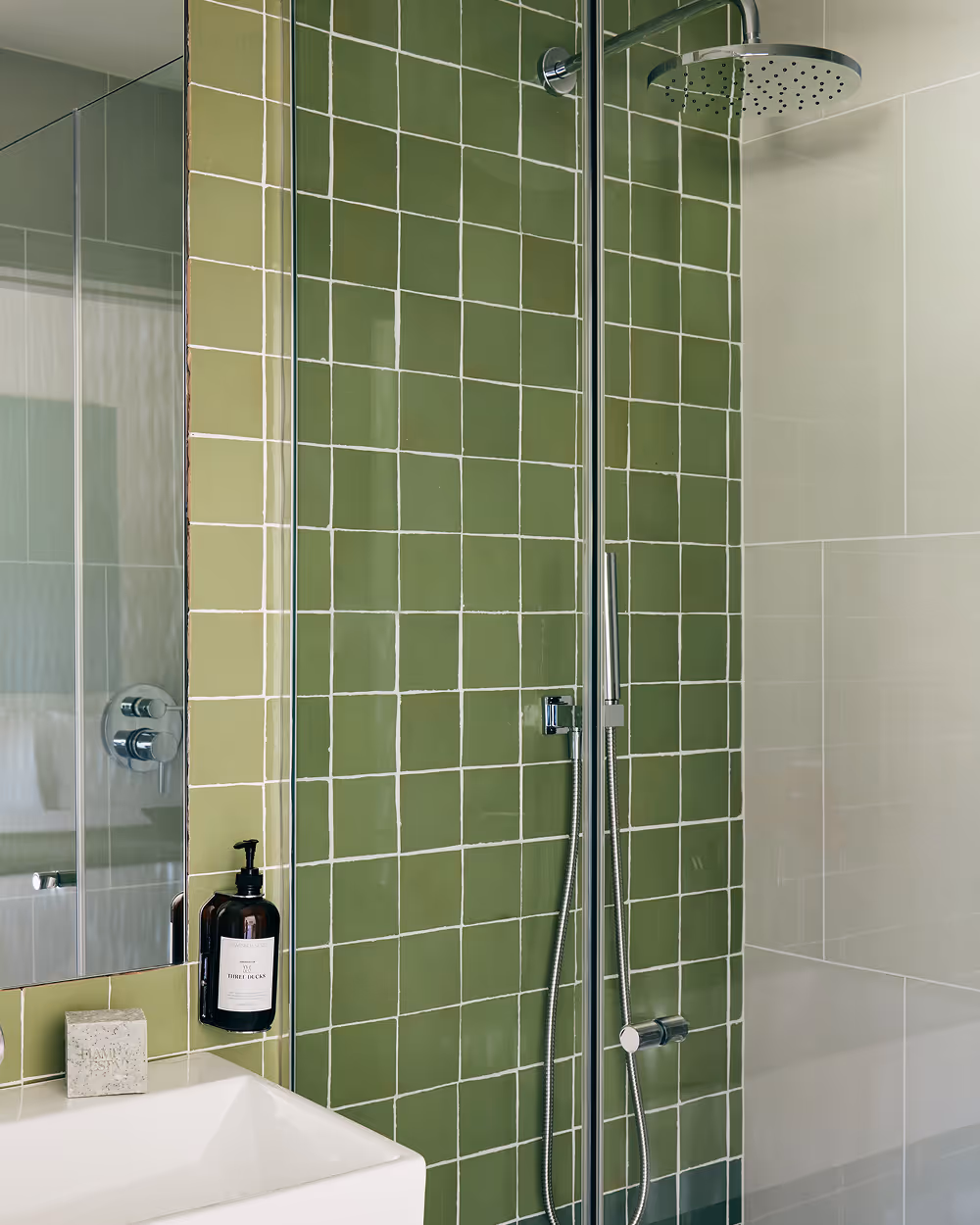 Green tiled shower next to white sink with mirror above it