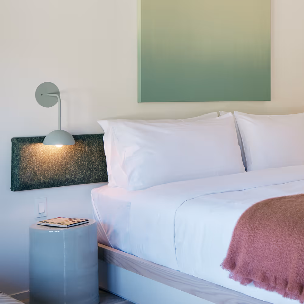 Angled view of king bed, side tables and sconces on either side, green painting above bed