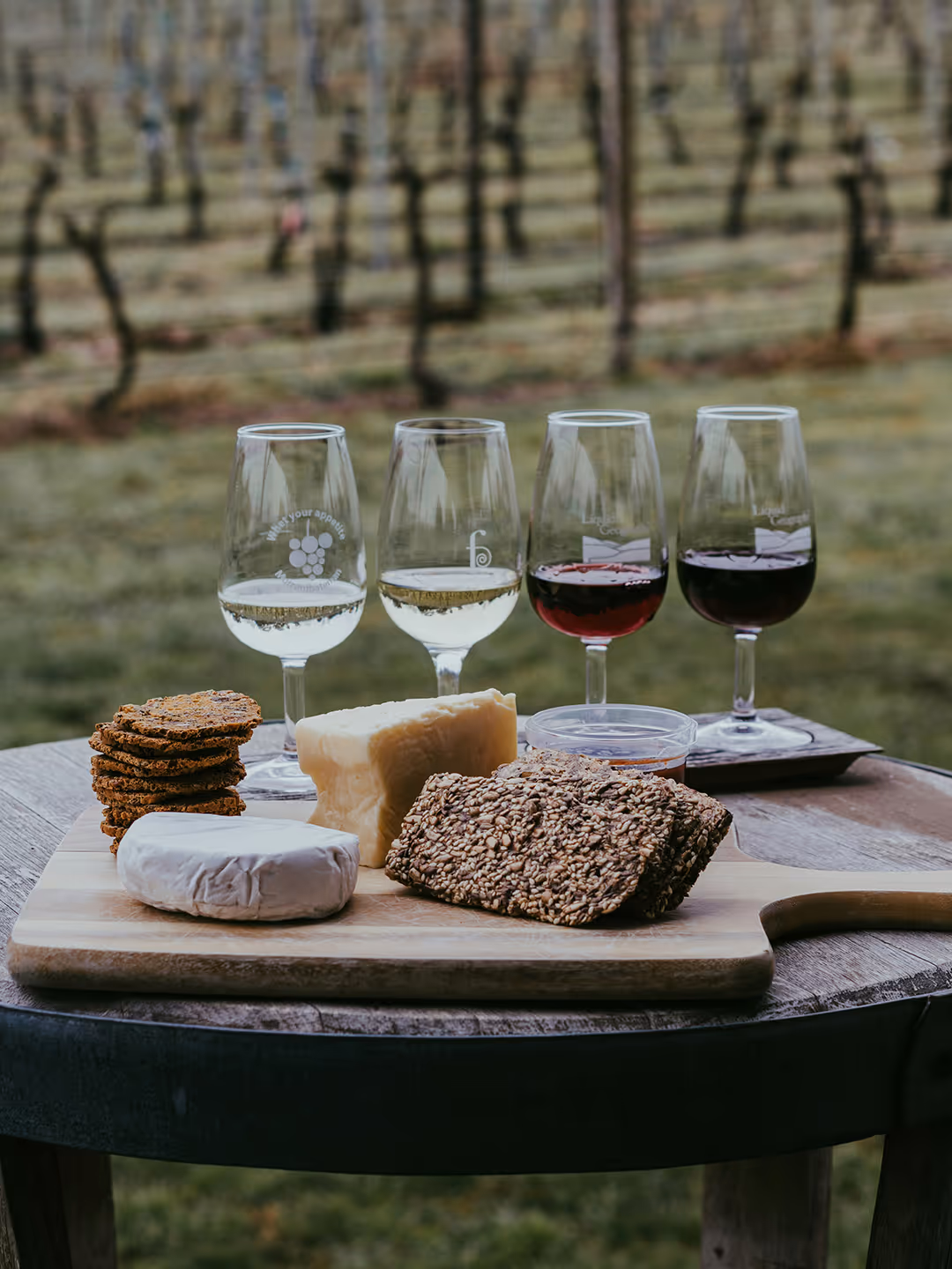 Four wine glasses and a tray of bread and cheese on a table outside
