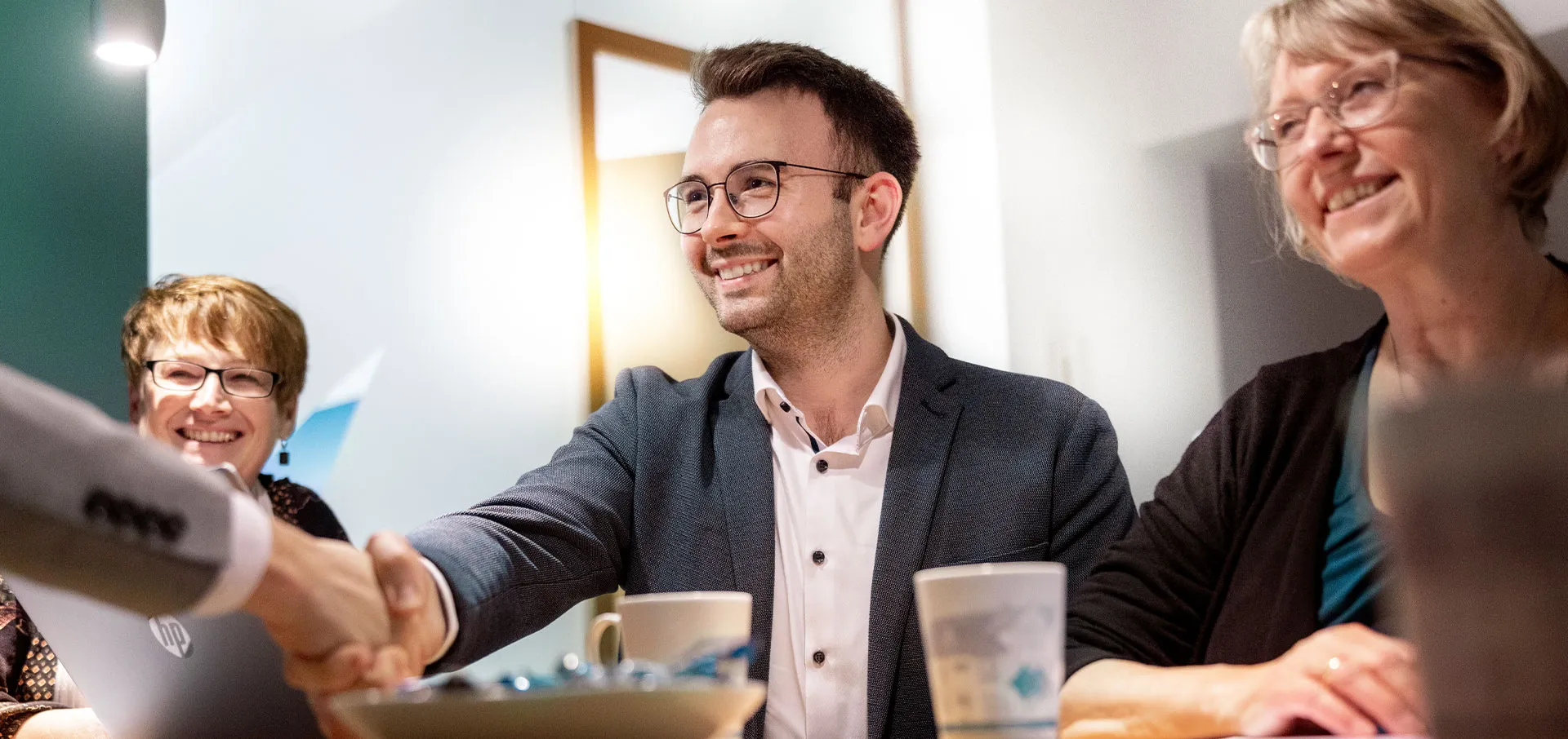 Vier Personen sitzen an einem Tisch, zwei schütteln sich die Hände