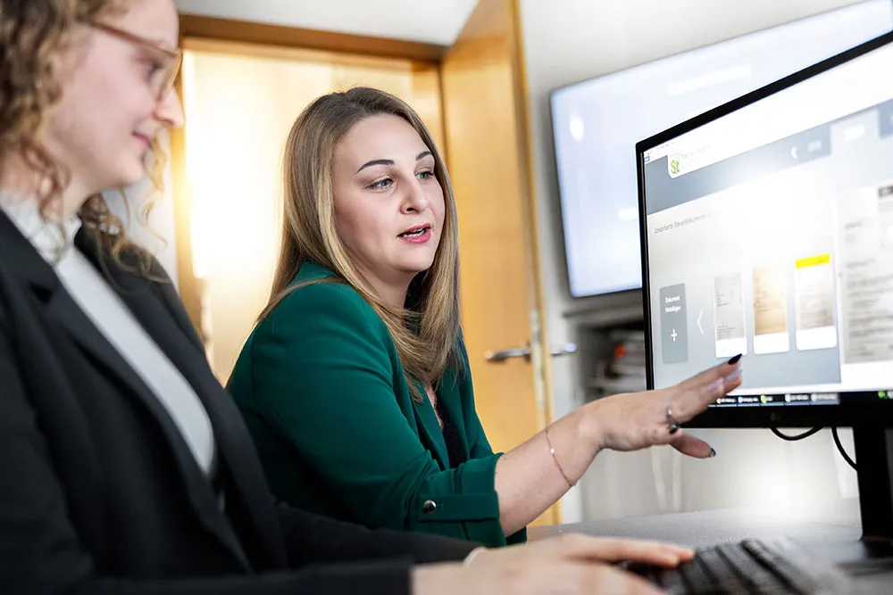 Zwei Frauen sitzen an einem Schreibtisch vor einem Computerbildschirm mit geöffnetem Programmfenster