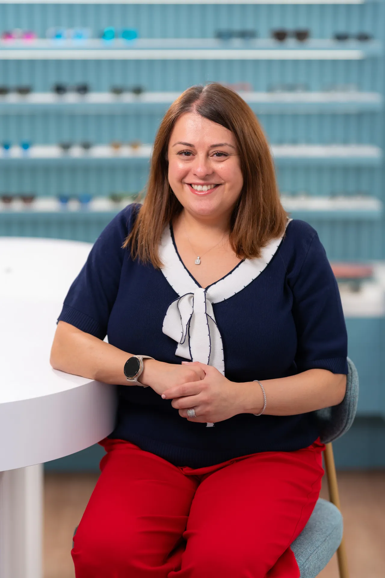Smiling professional woman in navy top and red pants sitting in office