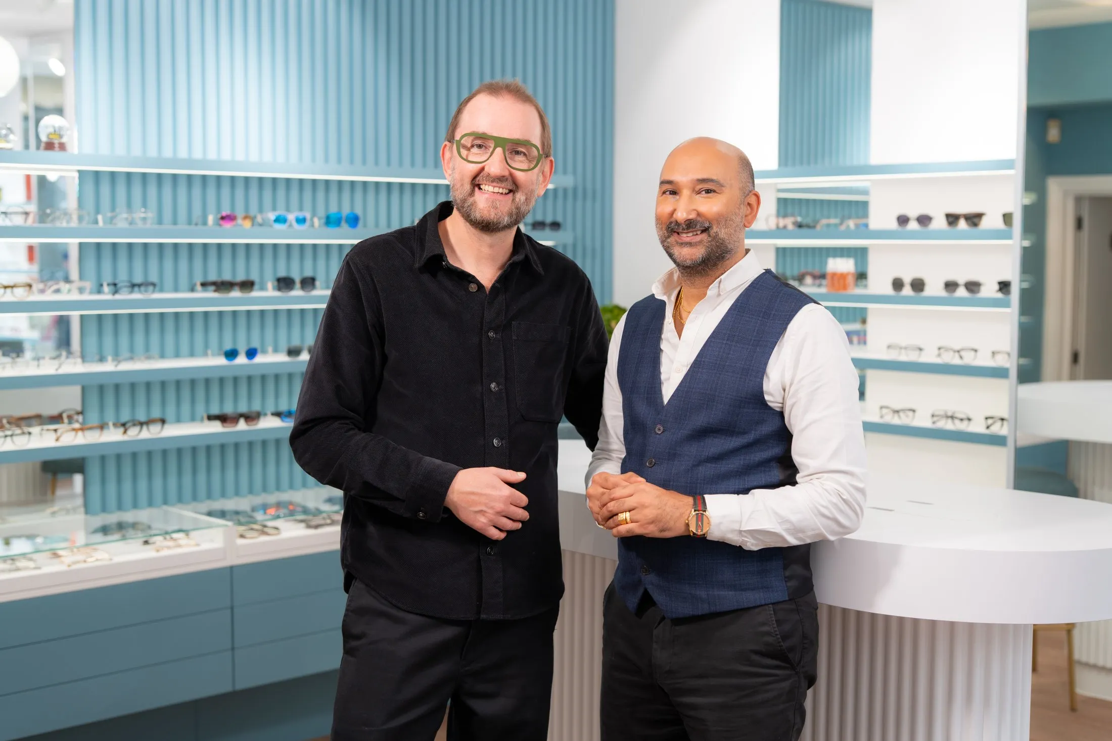 Two smiling business partners in optical store with eyeglass displays