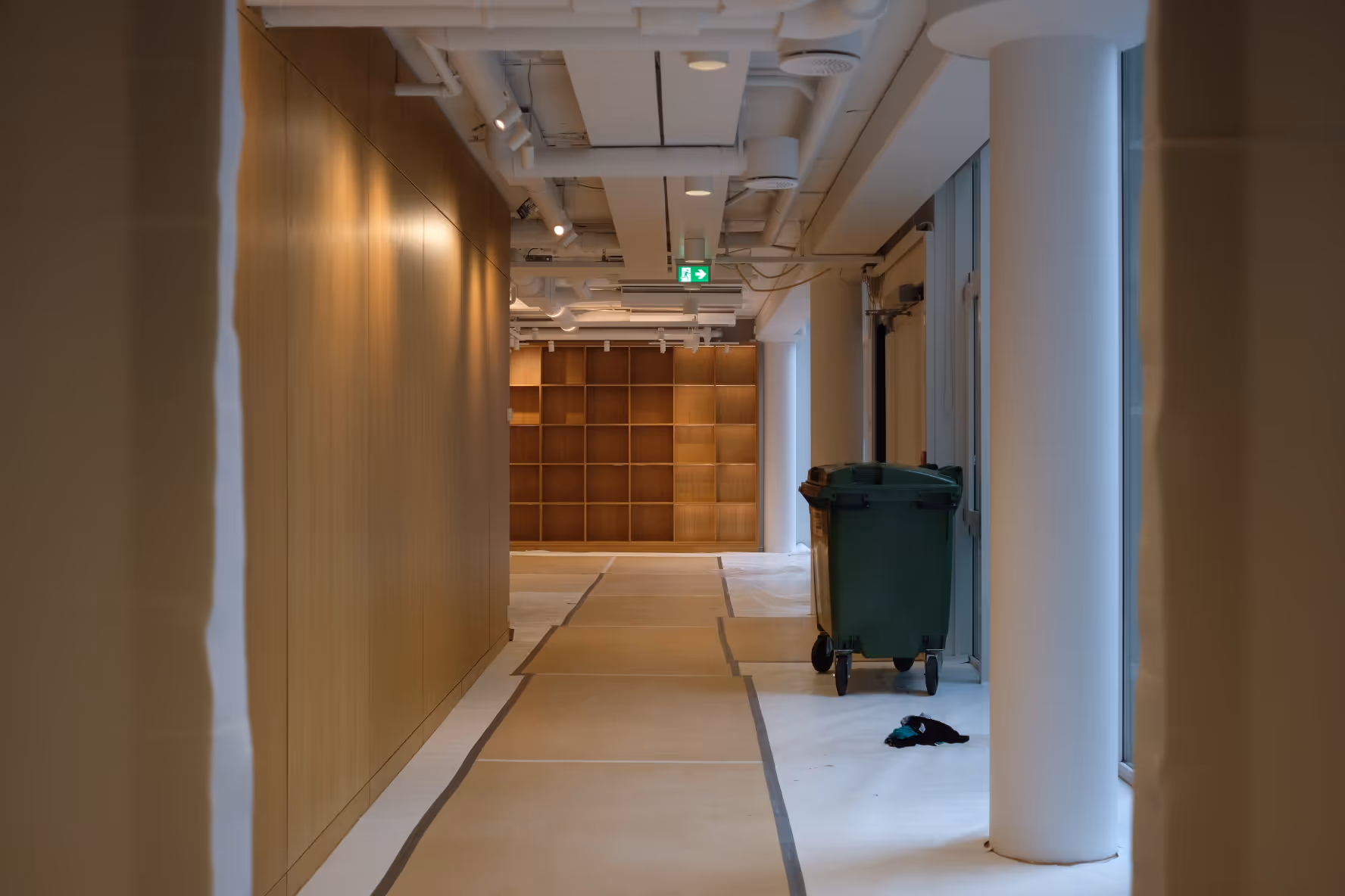 Moderne kontorbygg under ferdigstilling. En korridor med lyse tregulv dekket av beskyttelsesplast og tape før overlevering.