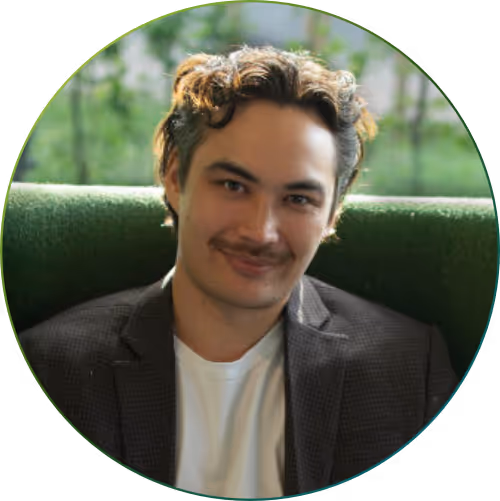 Mann mit kurzem braunem Haar und hellem Hemd trägt dunkelblauen karierten Blazer und lächelt in die Kamera.