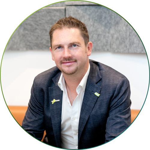 Mann mit kurzem braunem Haar und hellem Hemd trägt dunkelblauen karierten Blazer und lächelt in die Kamera.