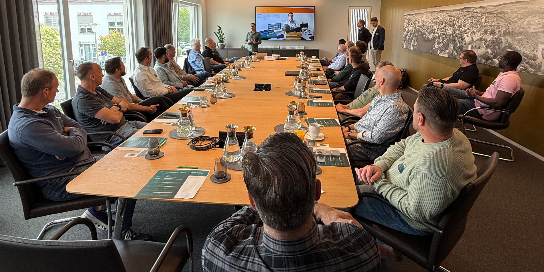 Sechs Geschäftsleute sitzen an einem runden Holztisch, trinken Kaffee und diskutieren Dokumente.