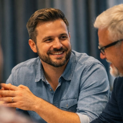 Ein lächelnder Mann in Hemd und Sakko steht vor einem Whiteboard und hält einen Marker.