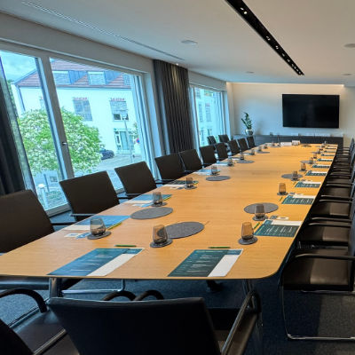 Frau liest konzentriert ein Dokument während eines Gesprächs mit zwei Personen in einem Büro.