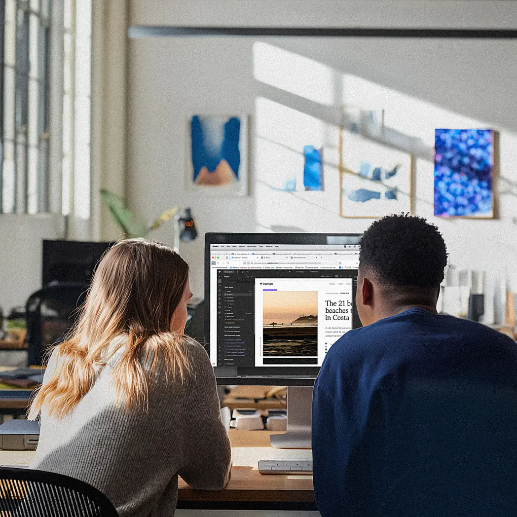 Two people sitting side by side looking at a desktop computer screen.