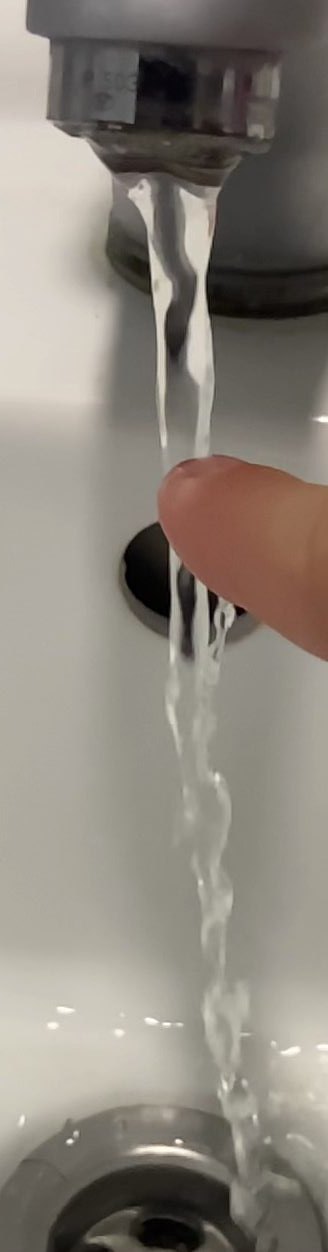A finger disrupting a stream of water from a tap, used as reference for the liquid stream effect