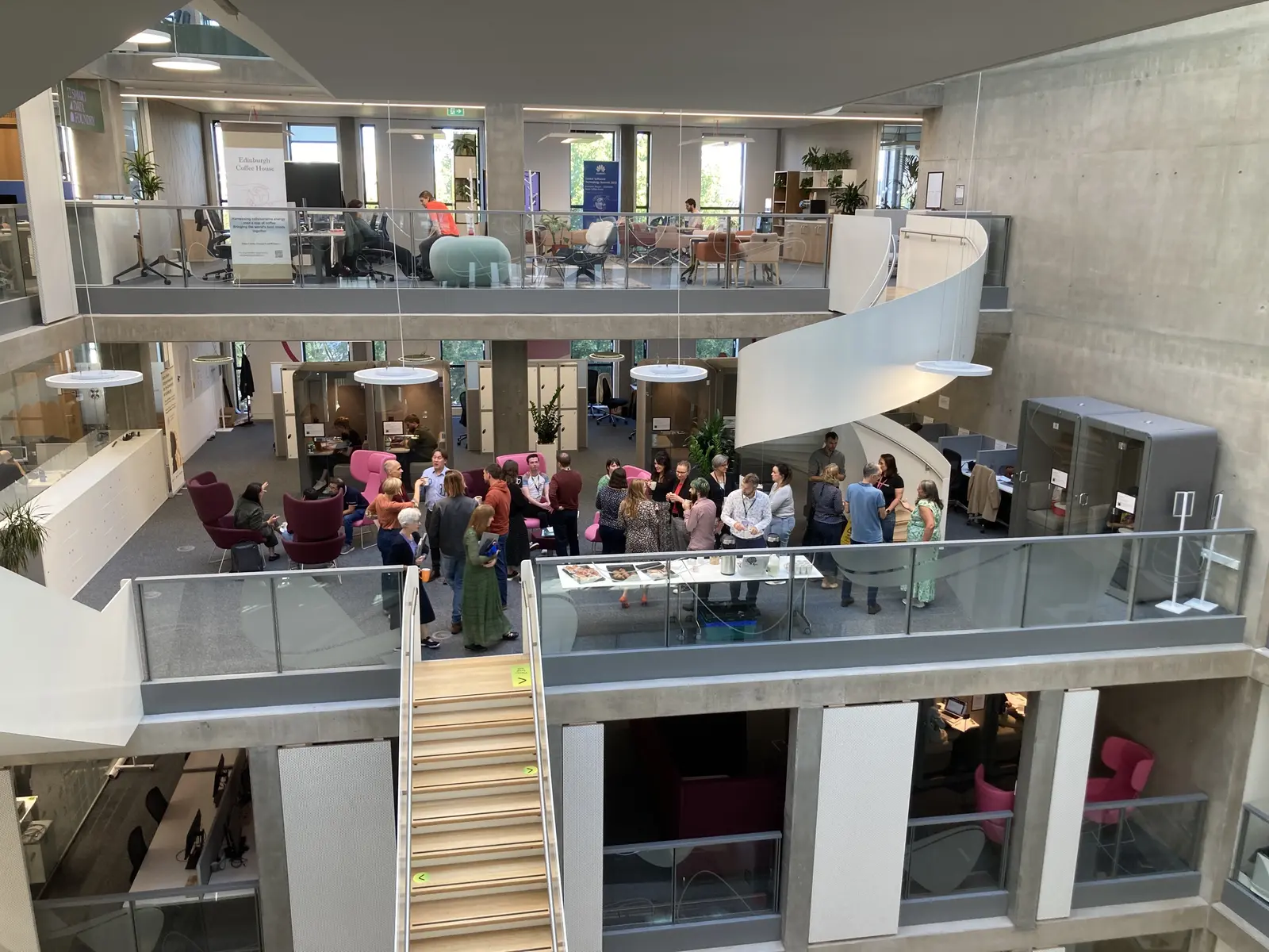 Group of people mingling on a mezzanine in a modern office building with a white spiral staircase and glass railings.