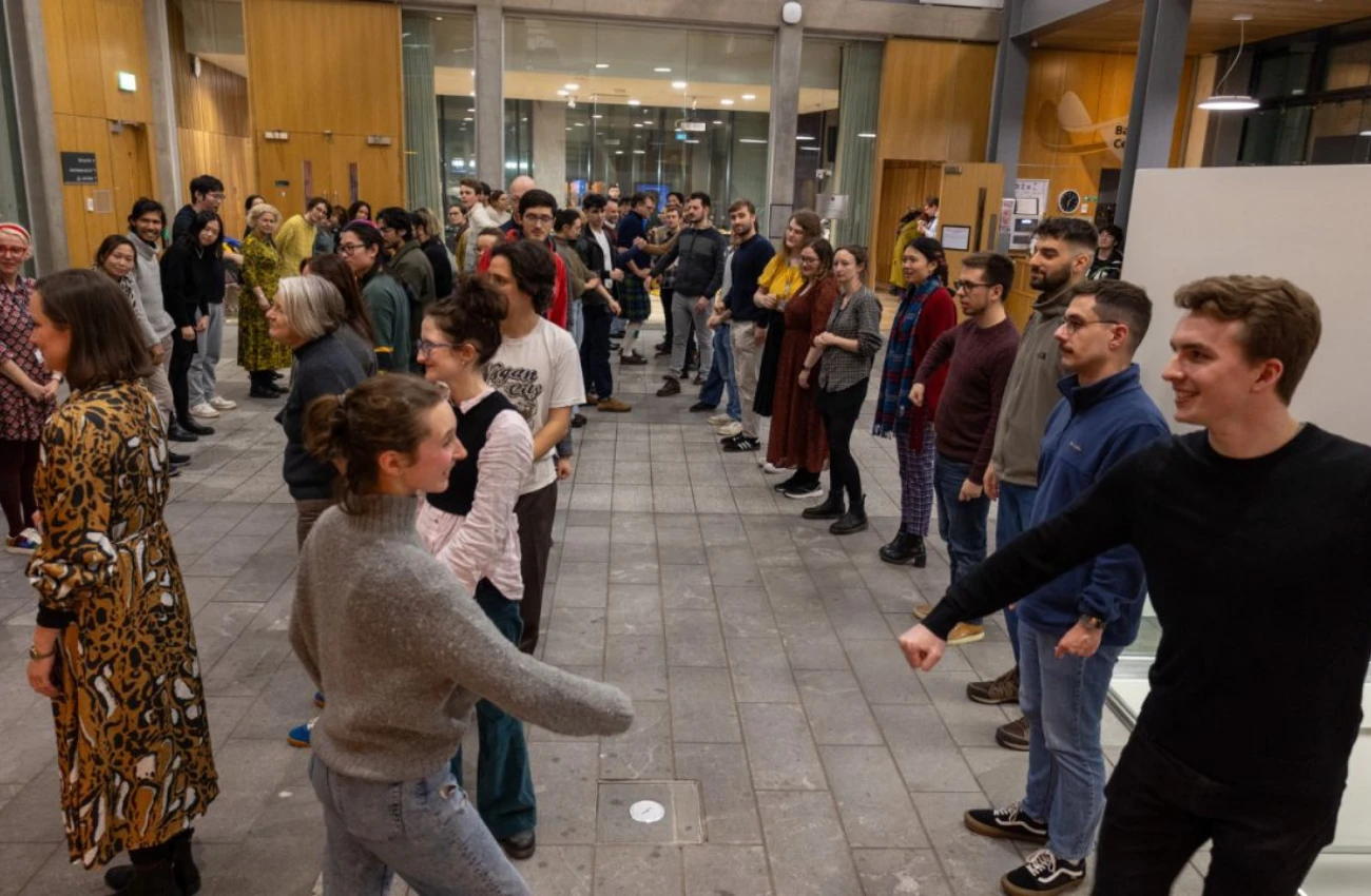 Large group of people standing in two lines facing each other inside a building, some extending arms for a handshake or fist bump.