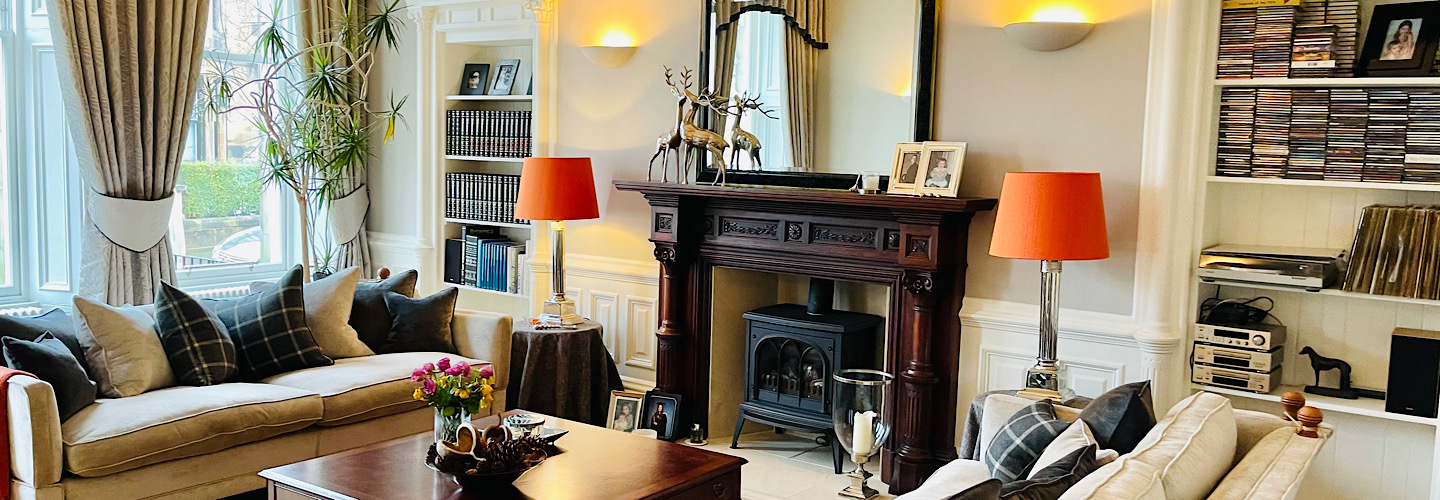 Cozy living room with beige sofas, orange lamps, decorative fireplace, and shelves with books and CDs.