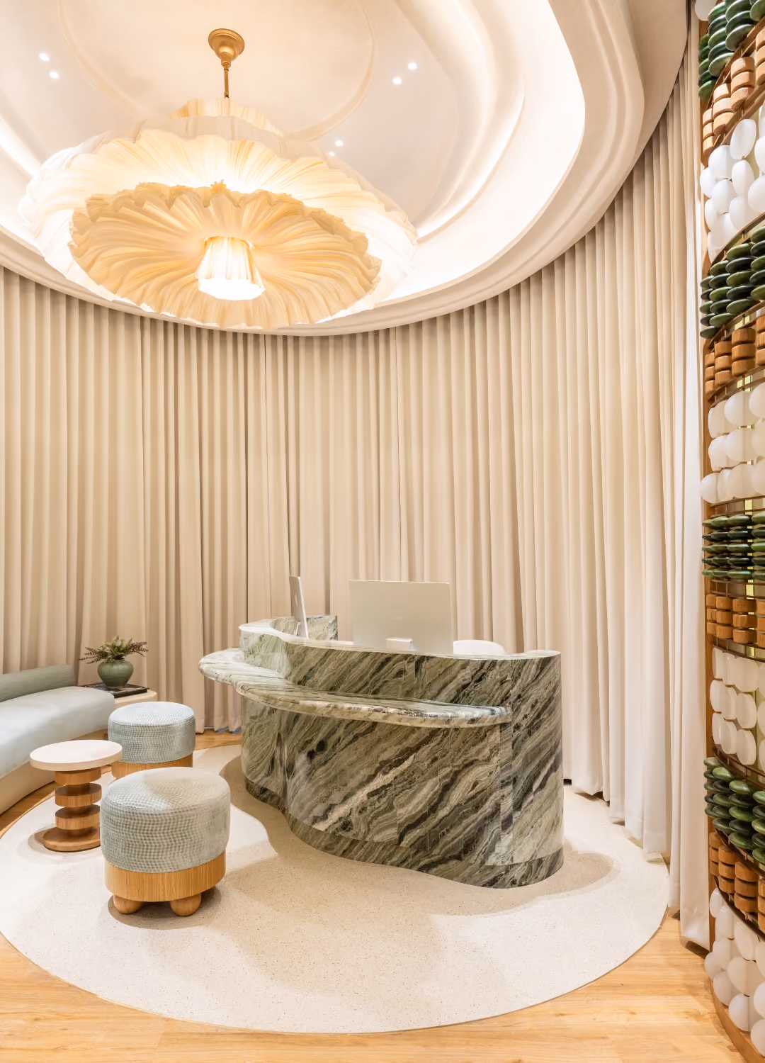 GenPrime Fertility Philippines clinic reception featuring a curved marble desk, sculptural ceiling light, soft green seating, and decorative wall panels.