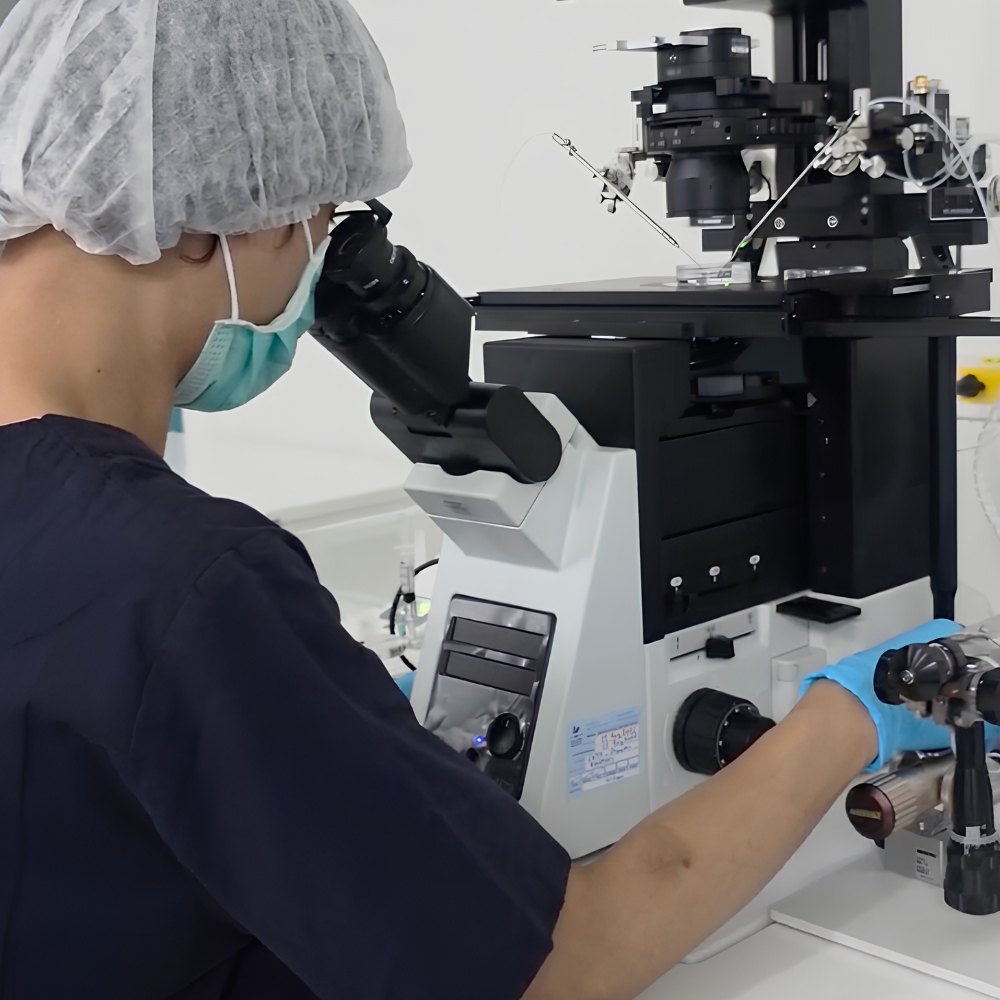Embryologist in protective equipment operating a micromanipulation microscope in a fertility laboratory.
