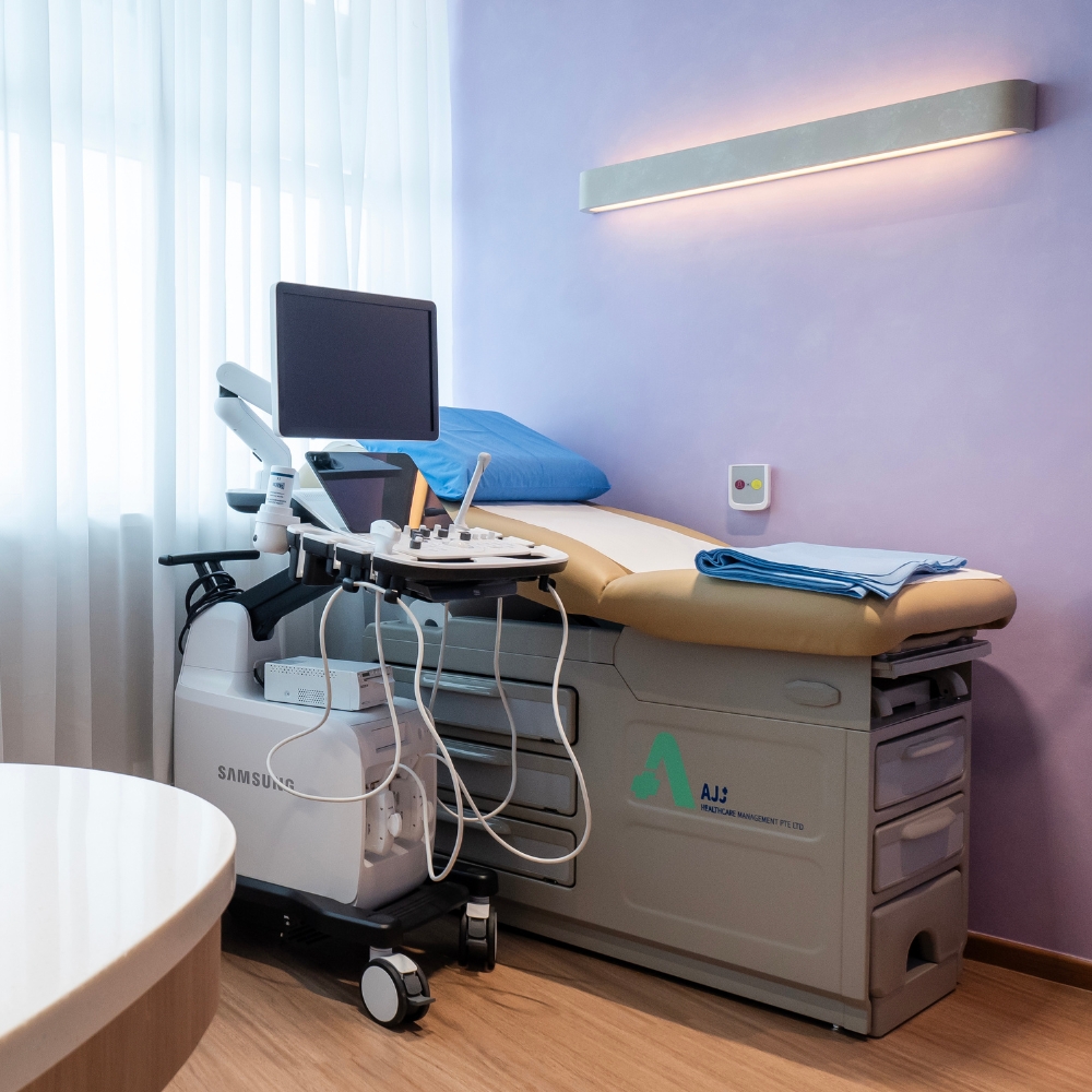 Ultrasound machine beside an adjustable examination bed in a bright GenPrime Fertility treatment room.