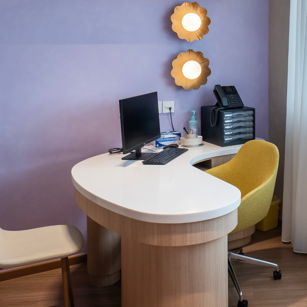 GenPrime Fertility consultation room with a curved desk, computer workstation, visitor seating, and warm floral wall lighting.